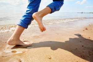 Pedorthist. Barefoot Child Running On Sandy Beach.