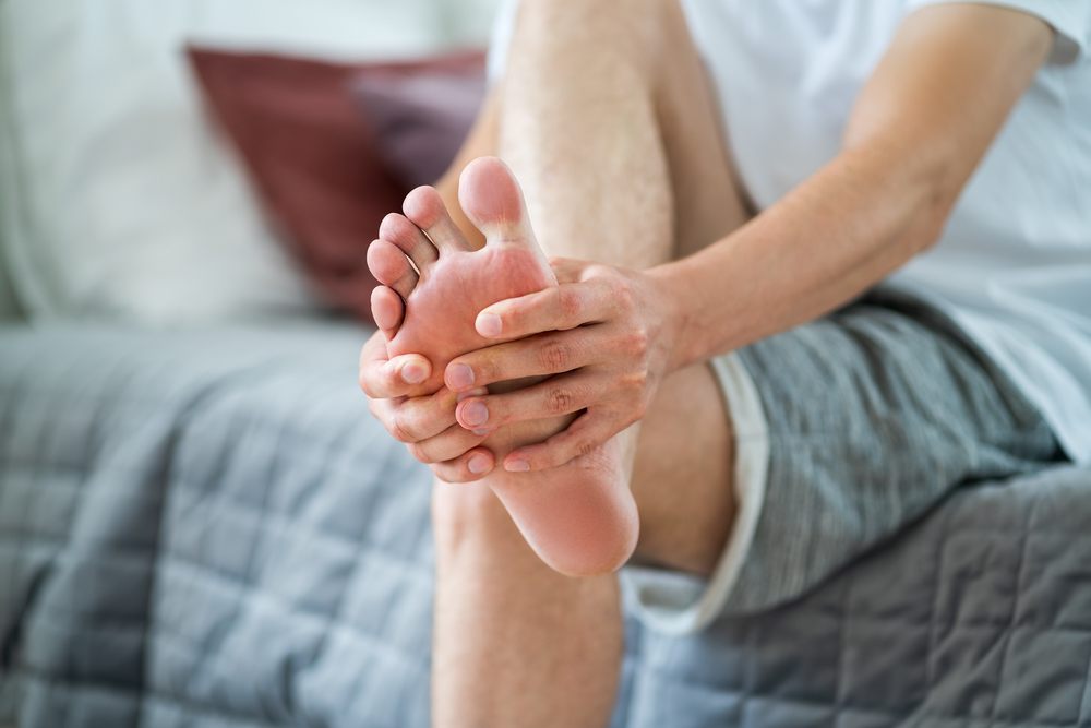 Are Pedorthist Services Covered by Insurance in Ottawa? Foot pain, man suffering from feet ache in home interior, podiatry concept.