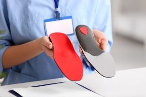 Custom Orthotics. A young female nurse is holding red orthopedic insoles in the clinic.