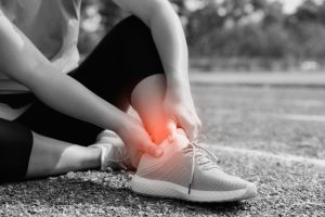 Can Ottawa Pedorthists Help Athletes With Injuries? A young woman is holding her ankle in pain with a red highlight on the stadium track. Broken twisted joint running sport injury. An athletic woman is touching her foot due to a sprain.