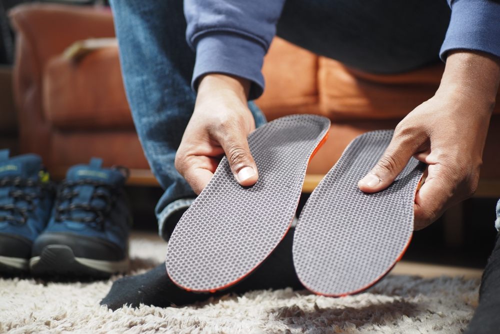 What Are Custom Orthotics? men hand putting Orthopedic insoles in shoes.