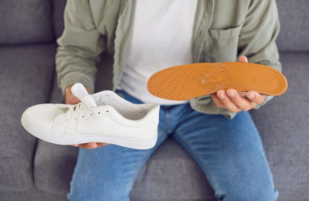 What Are Custom Orthotics? Close-up shot of a man inserting an insole into a shoe. Health-conscious action related to orthopedics or foot health, emphasizing the importance of proper footwear and orthotic care.