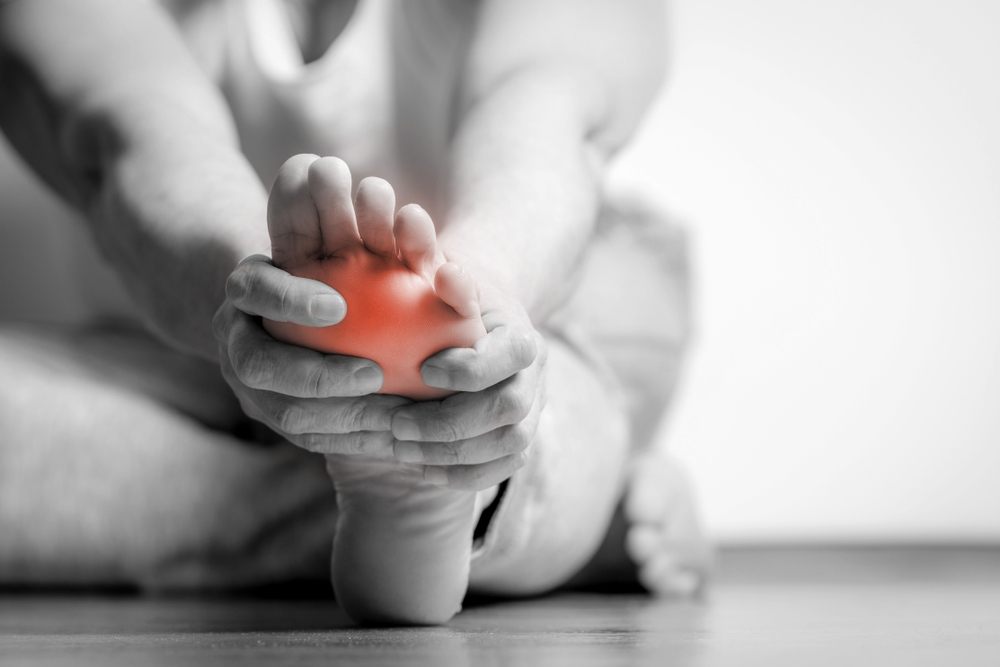 What Is Pedorthic Care? A Guide for Healthy Feet? Causian man holds hands to his painful feet, pain in foot. Black and white photography. red color is area of pain.