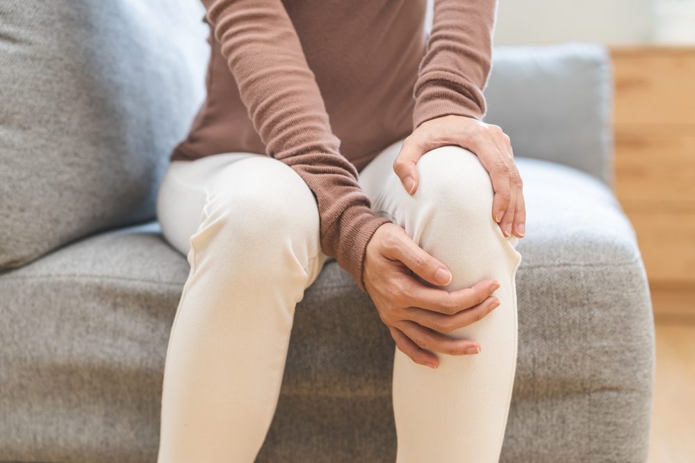 What Is Pedorthic Care? A Guide for Healthy Feet? Healthcare concept of knee pain: a close-up hand of a woman with a sore knee from standing all day at work.