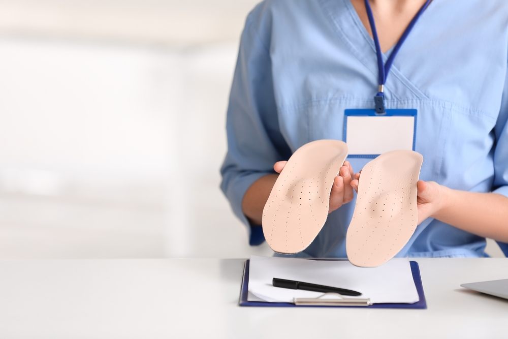 Custom Orthotics in Ottawa: A Complete Guide to Biomechanics, Foot Pain & Alignment. Young female nurse holding orthopedic insoles in clinic, closeup.