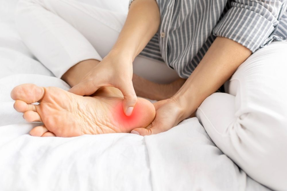 Step Into Comfort: Your Guide to Finding Orthopedic Shoes in Ottawa? A young woman feels pain when she presses on her heel and foot while sitting on the bed at home. Painful female legs from wearing uncomfortable, tight shoes and high heels, sprain, and arthrosis. Health concept.