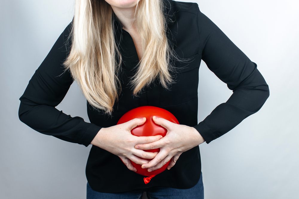 Why Am I Always Bloating? And What Can I Do About It? Bloating and flatulence concept. The woman holds a red balloon near her abdomen, which symbolizes bloating. Intestinal tract and digestive system. Problems with flatulence and the gastrointestinal tract.