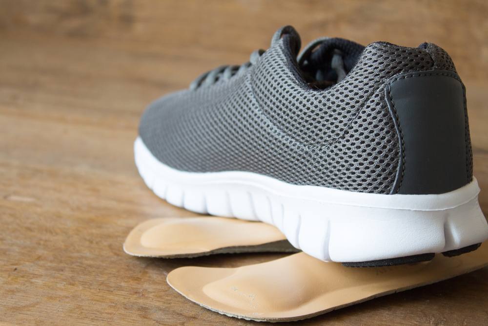 How to Choose the Best Orthopedic Shoes for Specific Foot Conditions. Gray running shoes with orthopedic insoles. Wooden board.